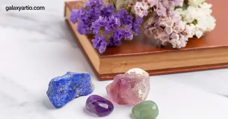 چند سنگ تزئینی روی سطح سفید کنار چند شاخه گل سفید و بنفش به عنوان تصویر مقاله سنگ های ماه تولد اسفند